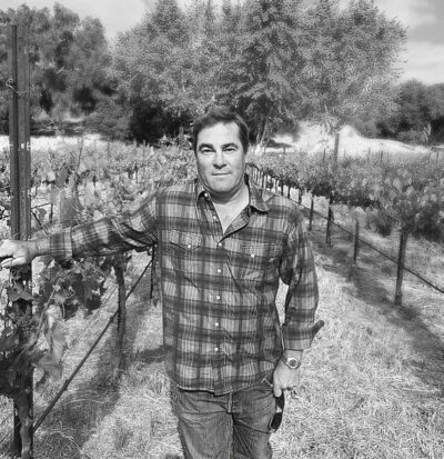 A black and white photograph of our esteemed winemaker, Justin Mund, standing in one of Monserate Winery's vineyards.