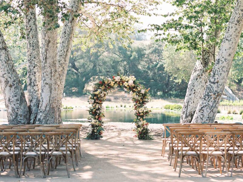 Monserate Winery's lakeside wedding venue in San Diego with a floral wedding arch standing between two giant sycamore trees.