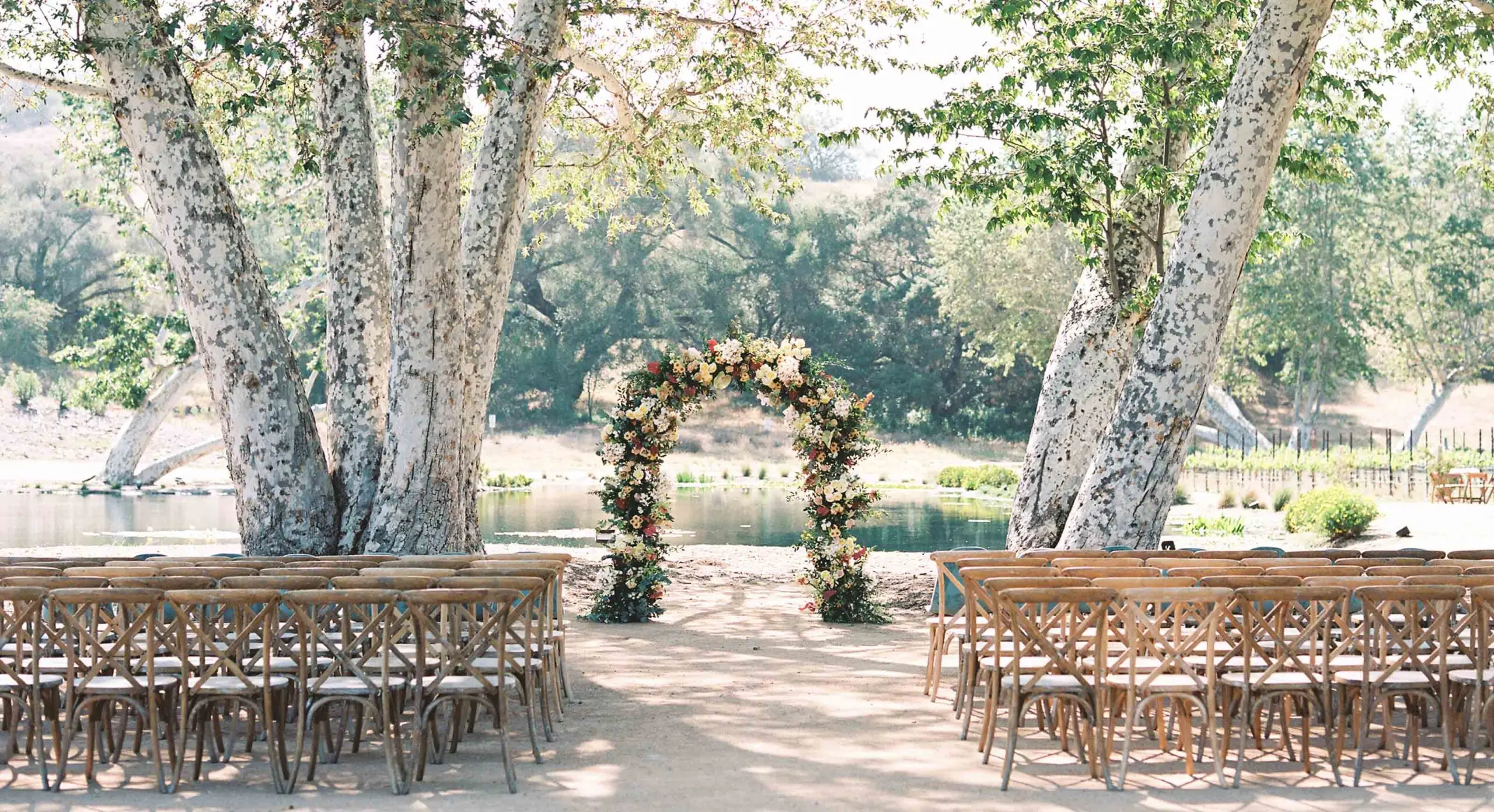 Monserate Winery's lakeside wedding venue in San Diego with a floral wedding arch standing between two giant sycamore trees.